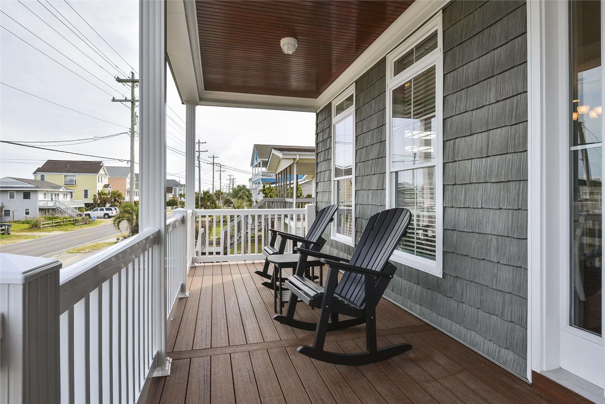 A wooden porch with two rocking chairs, a white railing, and a view of a residential street.