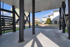 Ein überdachter Außenbereich mit Betonboden, Metallträgern und Blick auf Wohnhäuser im Hintergrund.