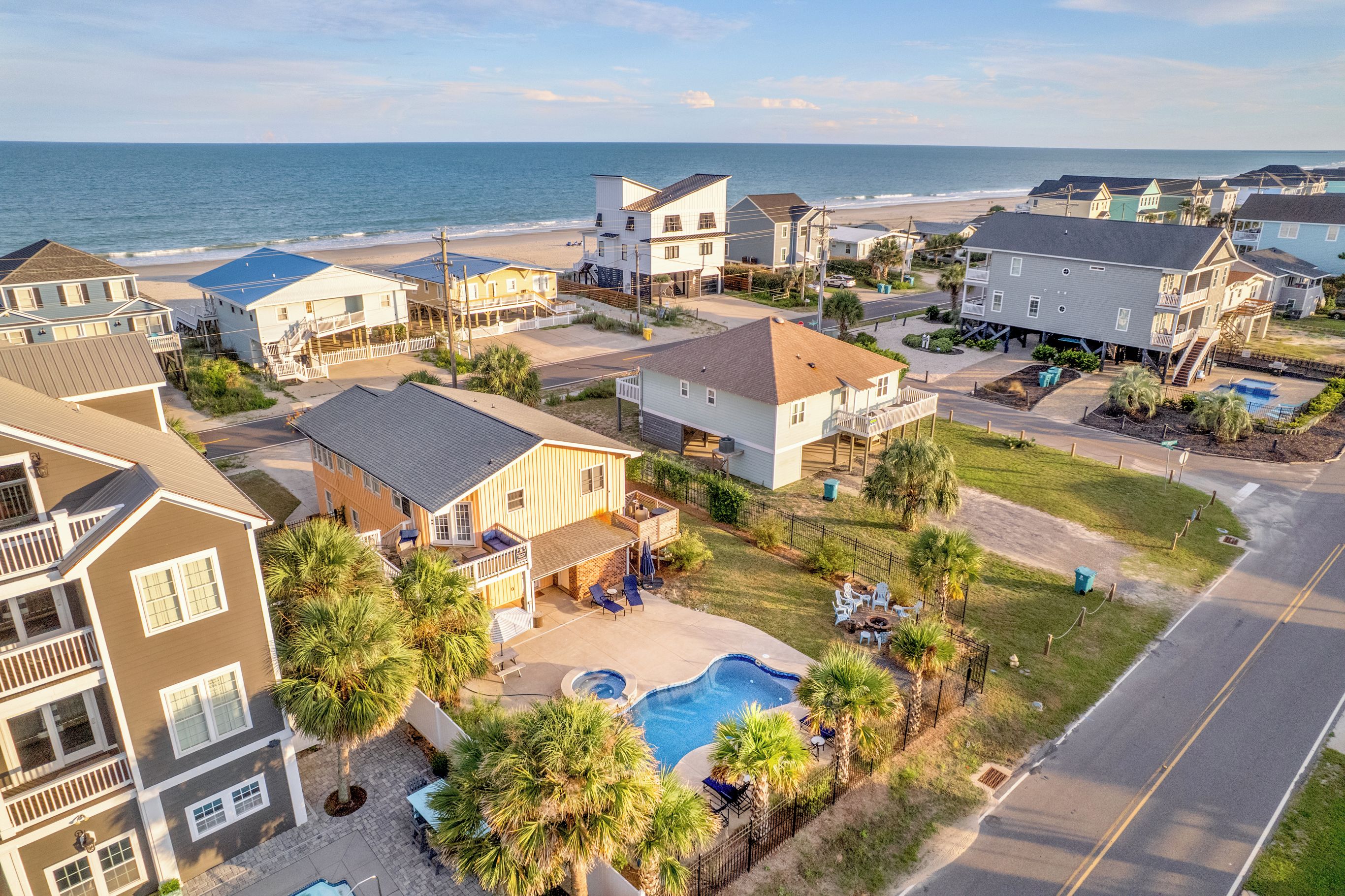 A residential area with houses, a swimming pool, and a beach in the background.
