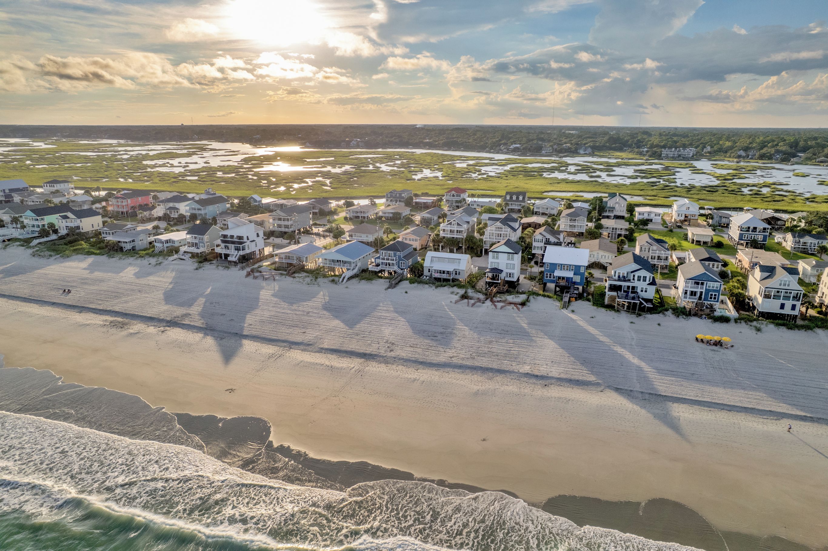 A coastal residential area with houses adjacent to the beach, featuring a sandy shoreline and waves.