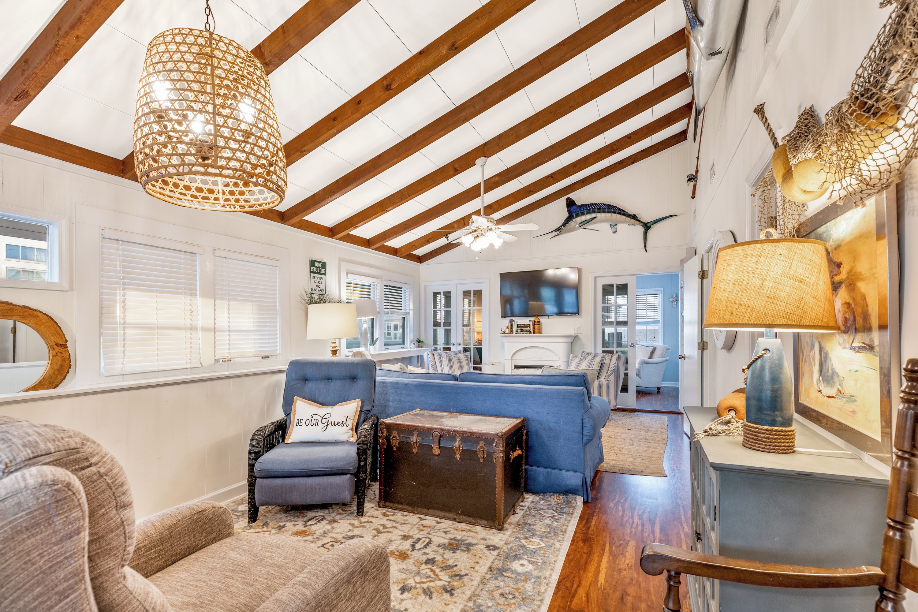 A spacious living room with a high ceiling, wooden beams, a large chandelier, and a mounted fish sculpture.