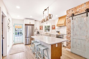 Una cocina moderna con una isla grande, electrodomésticos de acero inoxidable y una pared decorativa de ladrillo.