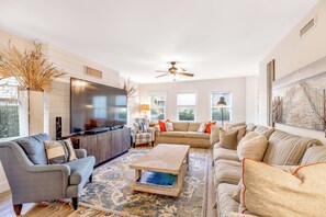 A spacious living room with a flat-screen TV, a ceiling fan, and a large window providing natural light. - Good Ol' Days: Private Pool, Hot Tub & Steps to the Beach (Murrells Inlet)