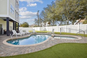 A swimming pool with a brick border, surrounded by a grassy area and a white fence. - Key Lime Pie: Ocean Views, Pool, Steps to Beach (Murrells Inlet)