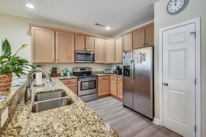 A kitchen with granite countertops, wooden cabinets, stainless steel appliances, and a clock on the wall. - La Casa Di Famiglia: Coastal Retreat, Private Pool & Steps to the Sand (Surfside Beach)