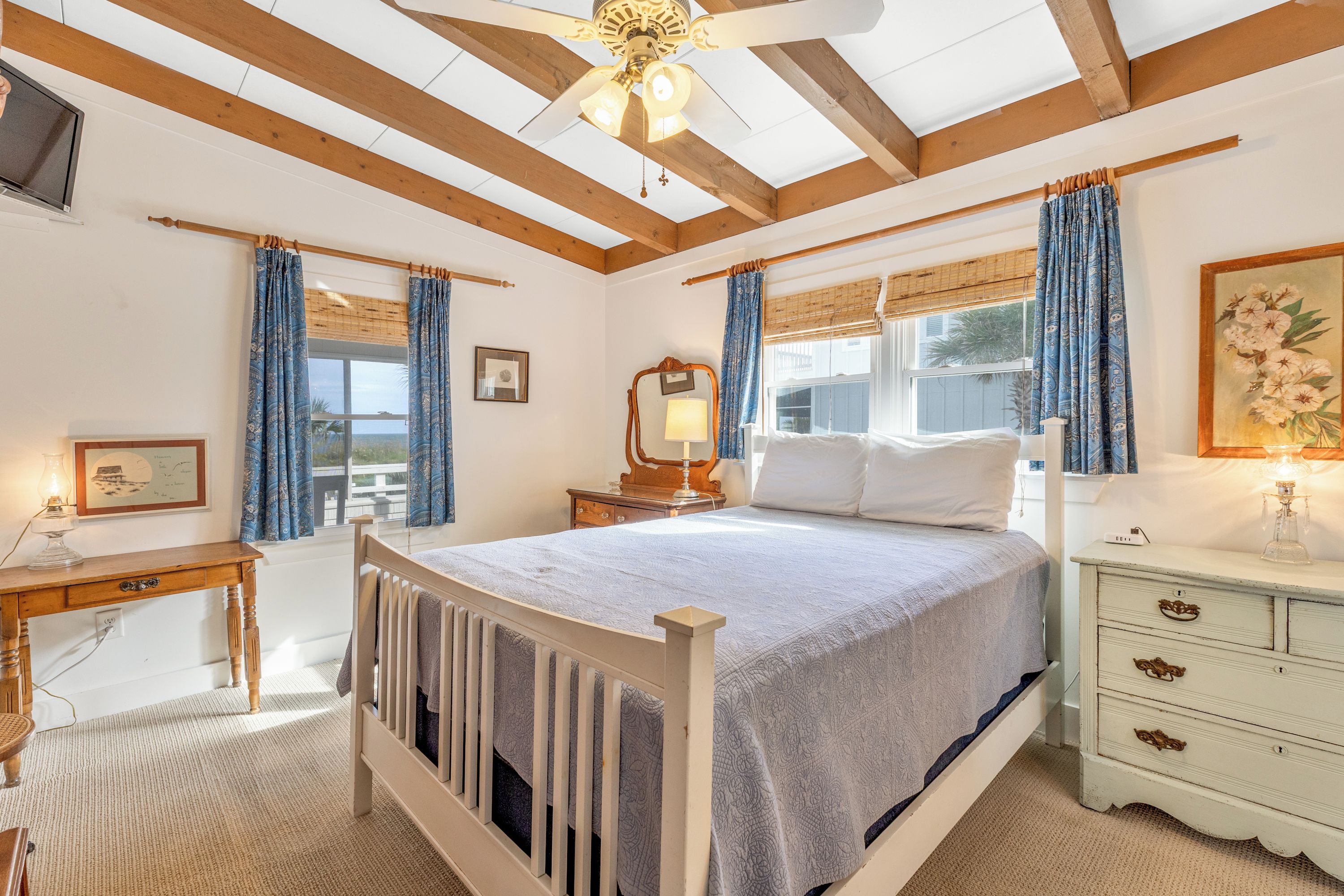 Une chambre avec un plafond en bois, un lit recouvert de draps blancs, une table de chevet avec une lampe et une commode avec des tiroirs.