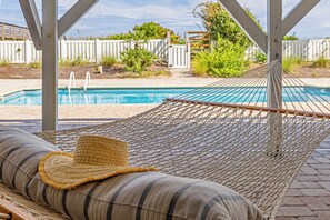 A hammock with a striped cushion and a straw hat, overlooking a swimming pool. - Panacea: Oceanfront Charm with Pool, & Private Beach Walkway (Murrells Inlet)
