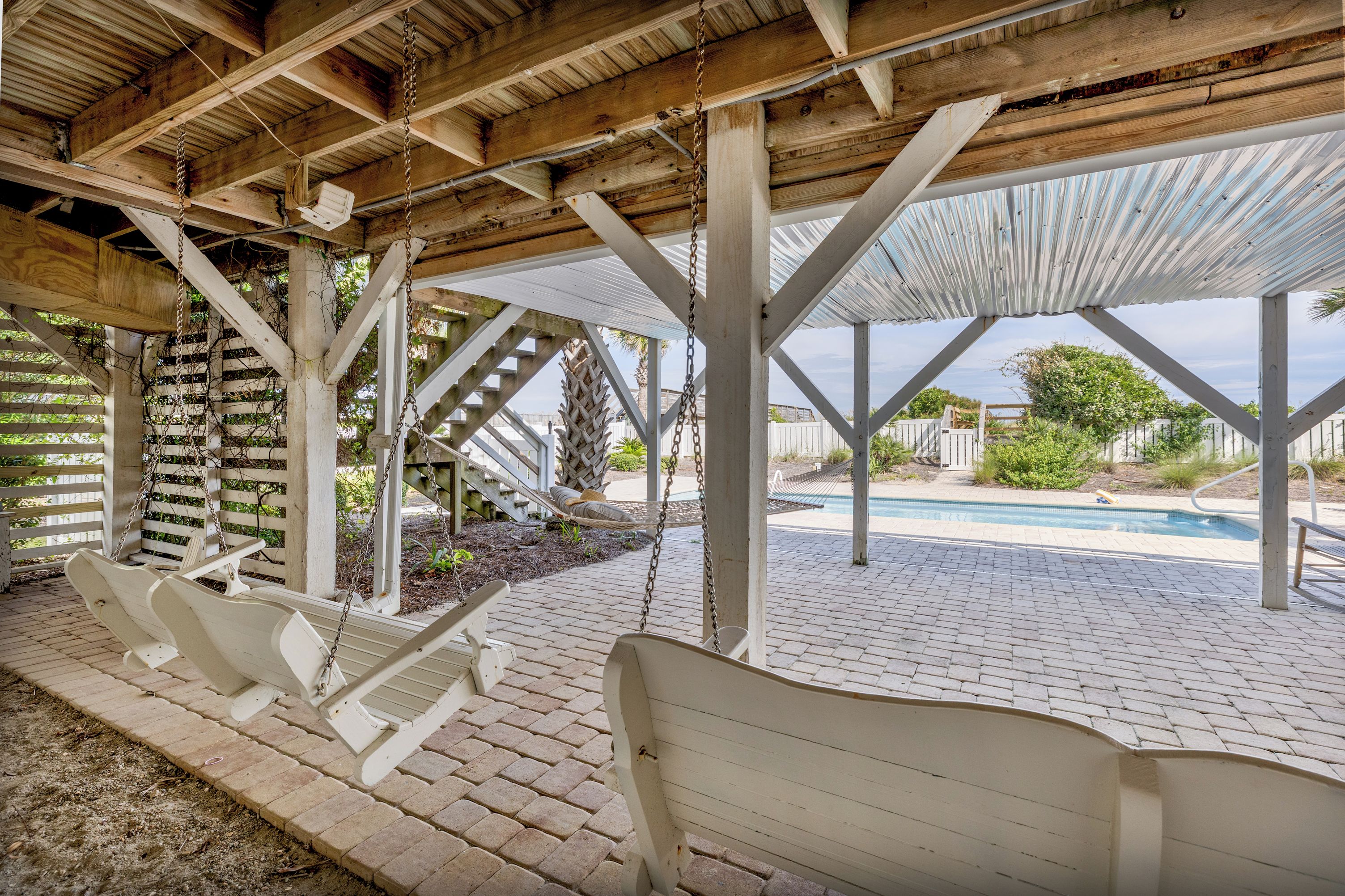 A covered outdoor area with a pool, wooden benches, and a pergola structure.