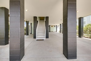 Ein überdachter Gang mit einer zentralen Treppe, gesäumt von Säulen, der zu einem Gebäudeeingang führt.