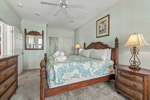 A bedroom with a bed, a dresser, a nightstand, a ceiling fan, a mirror, and a painting on the wall. - Peachy Keen: Private Pool, Ocean Views & Steps from the Sand (Murrells Inlet)