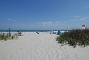 A sandy beach with a clear sky, a sign indicating to keep off dunes, and a few people and umbrellas in the distance. - Quality Time: Private Pool Retreat Just Steps from the Beach (Murrells Inlet)