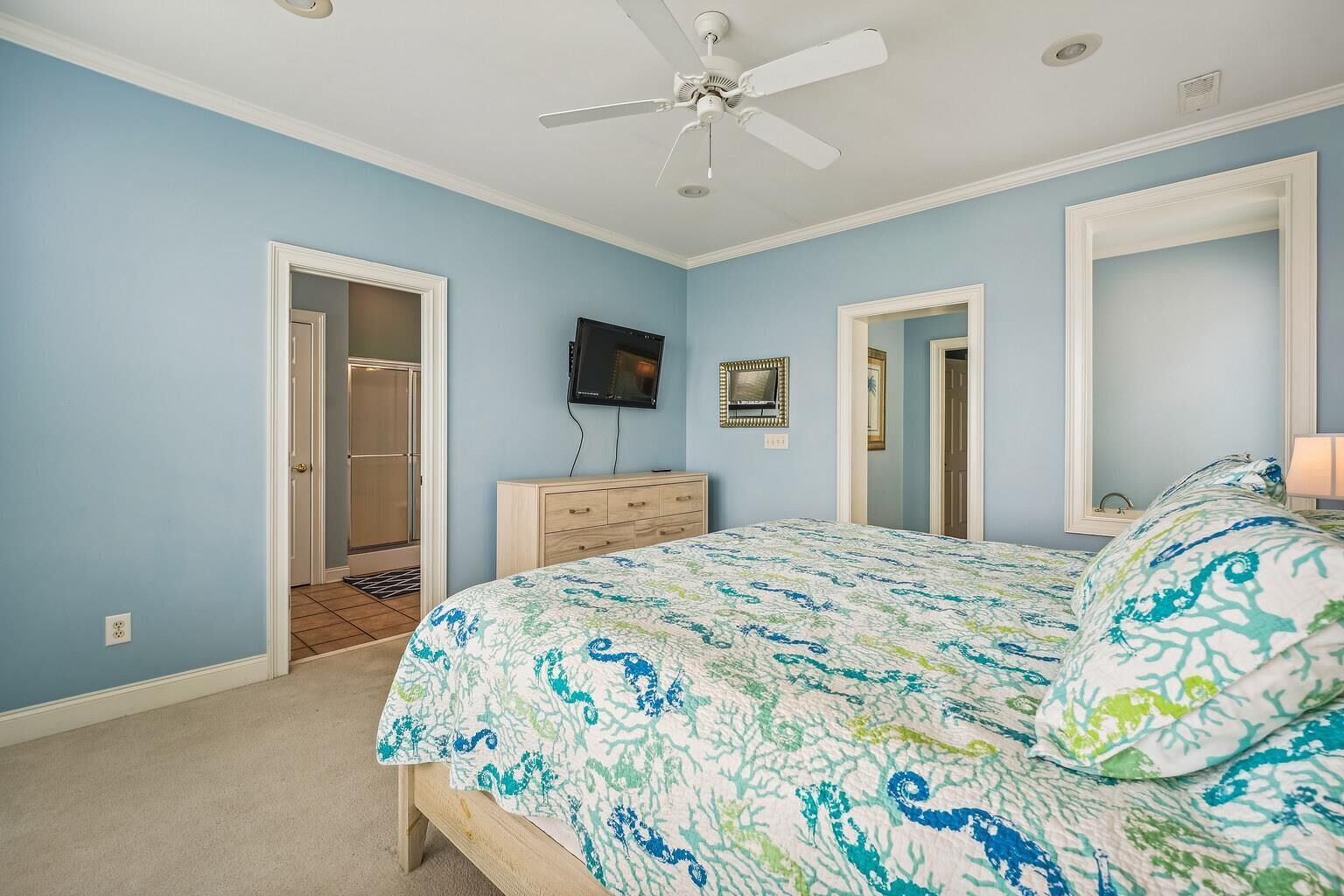 Une chambre à coucher comprenant un lit, un ventilateur de plafond, un téléviseur et une commode.