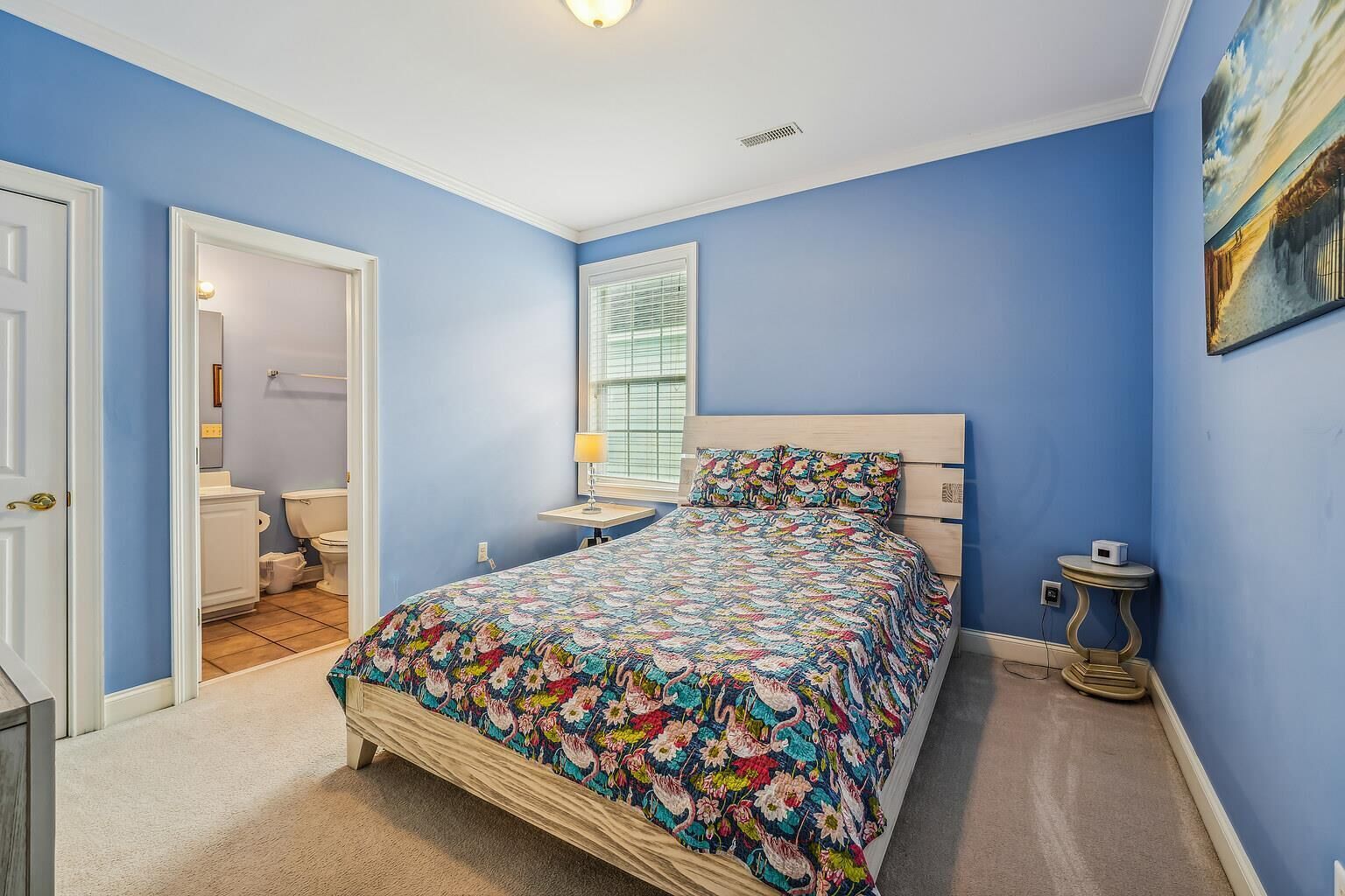 A bedroom with a bed, a bedside table, a lamp, and a painting on the wall.