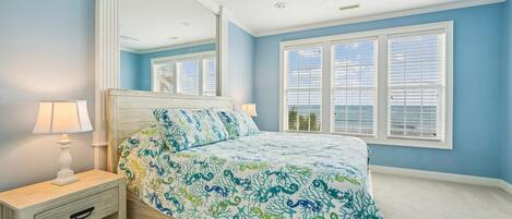 A bedroom with a bed, nightstand, lamp, ceiling fan, and large windows.