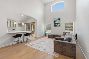 A modern living room with a sofa, chairs, and a rug. There is a kitchen area with a counter and bar stools. - 5BR Private Pool Retreat  Near Disney (Kissimmee)