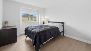 Una camera da letto con un letto, un comodino, una lampada e una finestra che dà su un edificio.