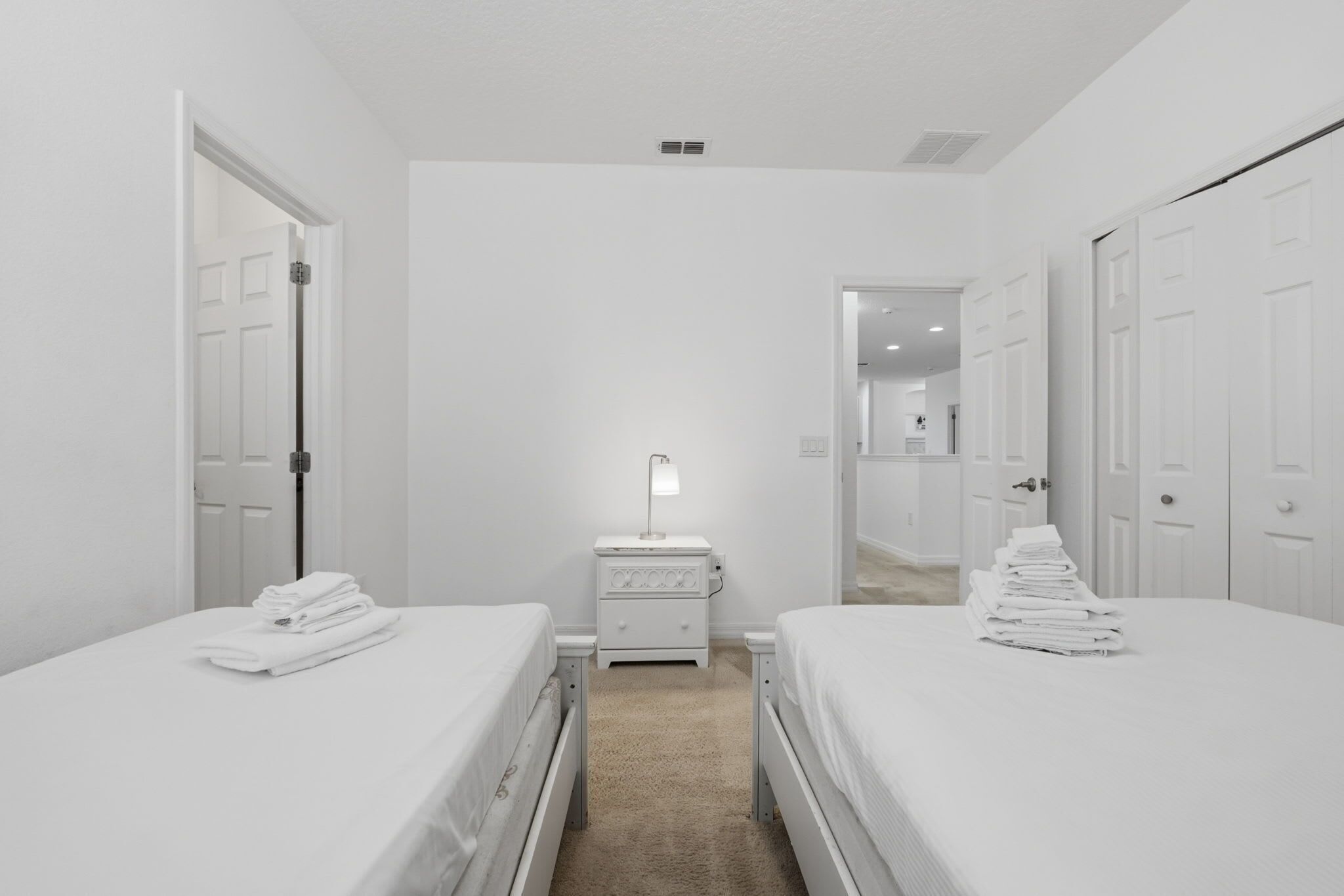 Une chambre d’hôtel avec deux lits, une table de chevet avec une lampe et une porte donnant sur une autre pièce.