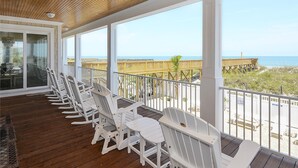Een overdekt terras met witte stoelen en uitzicht op het strand.
