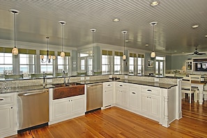 A spacious kitchen with a large island, white cabinetry, and a view of the ocean through large windows. - Sea La Vie: Oceanfront Retreat, Private Pool & Game Room (Murrells Inlet)