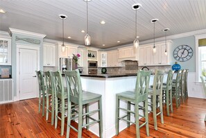 A kitchen with a central island, bar stools, and a clock on the wall. - Sea La Vie: Oceanfront Retreat, Private Pool & Game Room (Murrells Inlet)