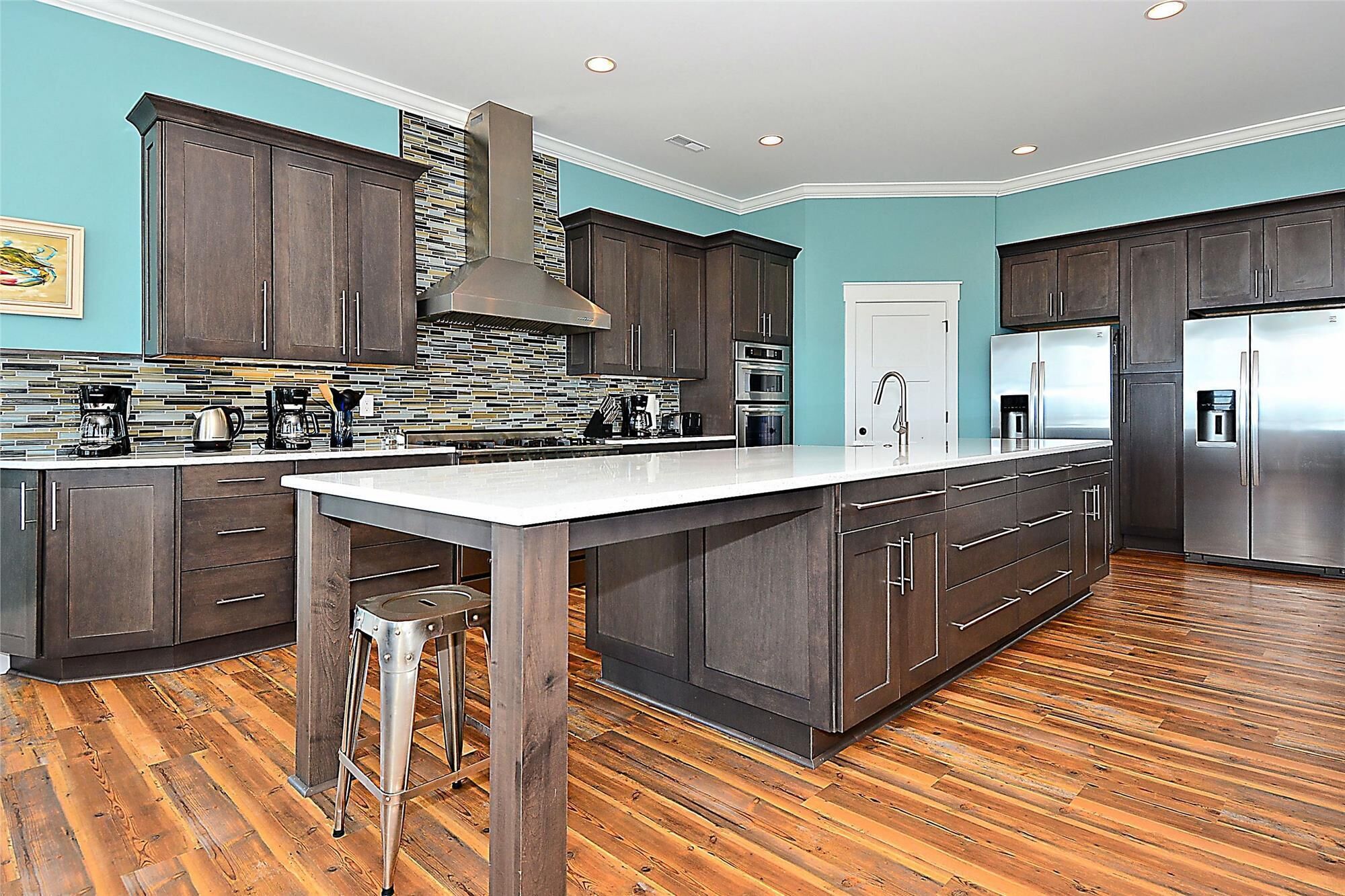 A modern kitchen with dark wood cabinets, a large island, stainless steel appliances, and a herringbone tile backsplash.