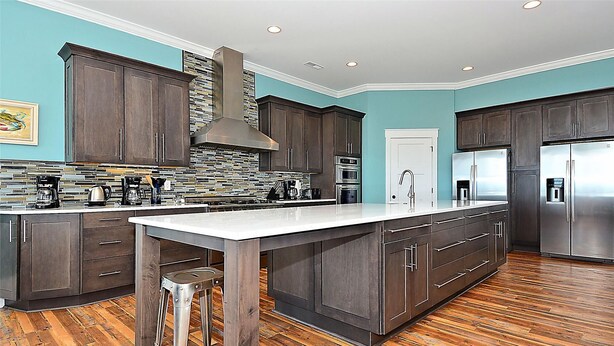 Una cocina moderna con alacenas de madera oscura, una isla grande, electrodomésticos de acero inoxidable y un revestimiento de baldosas en espiga.