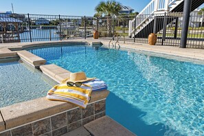 A clear swimming pool with a stone edge, a towel, sunglasses, and a straw hat on the edge. - William's Wharf: Inlet Front, Dock, Pool & Steps to the Beach (Murrells Inlet)