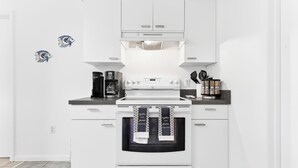Una cocina moderna con armarios blancos, horno empotrado, cafetera y hervidor.