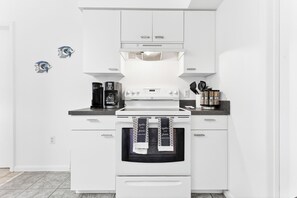 Eine moderne Küche mit weißen Schränken, einem Backofen, einer Kaffeemaschine und einem Wasserkocher.