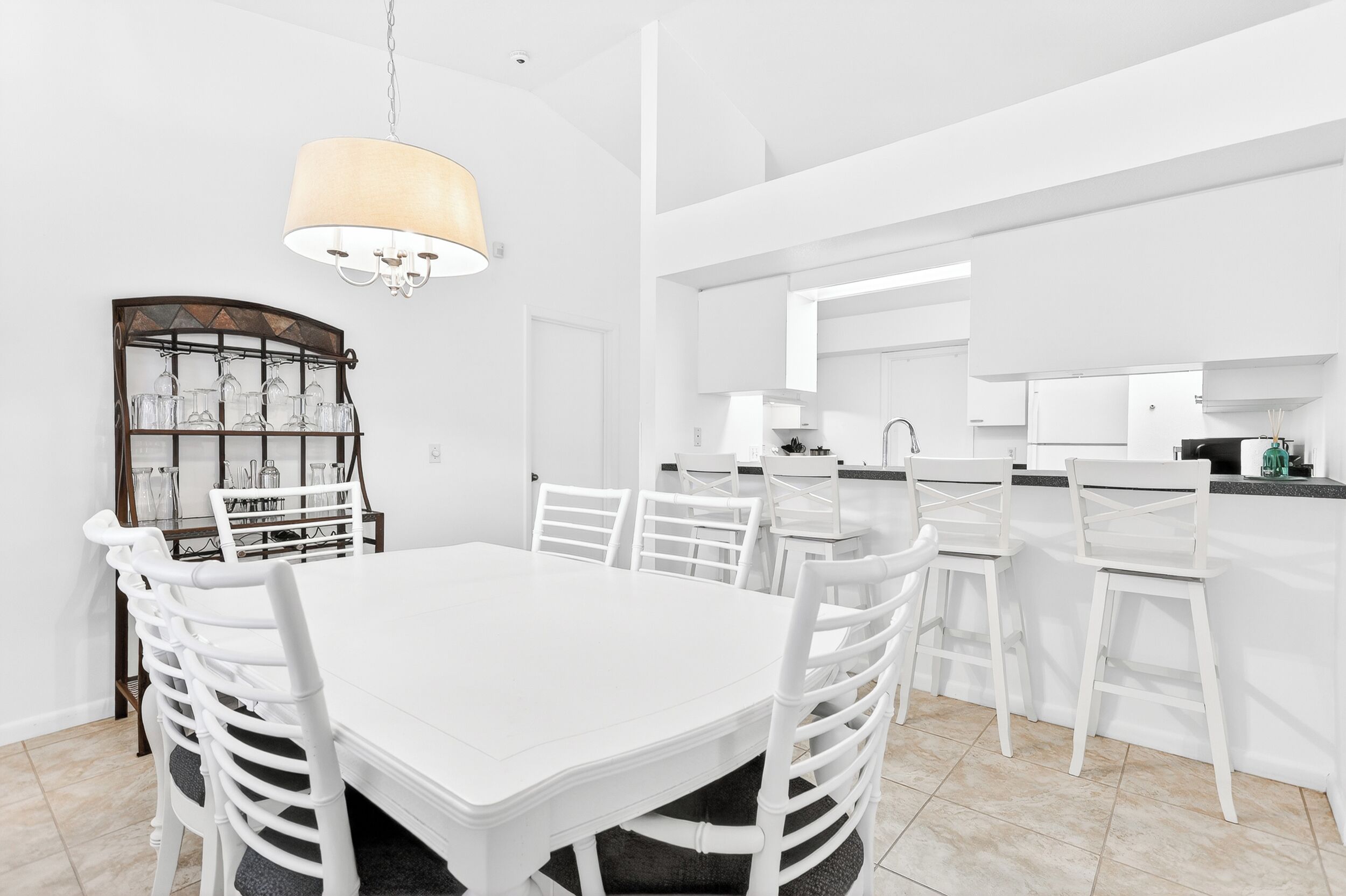 A modern kitchen with white cabinetry, a dining area with a white table and chairs, and a chandelier.
