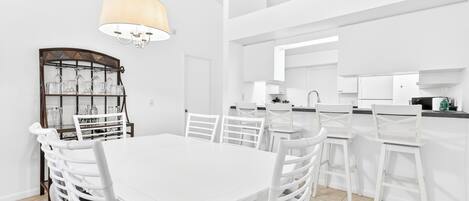 A modern kitchen with white cabinetry, a dining area with a white table and chairs, and a chandelier.
