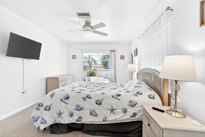 A bedroom with a bed, a ceiling fan, a TV mounted on the wall, a bedside lamp, and a window with blinds. - Rotonda West Getaway | Private Heated Pool Retreat (Rotonda West)