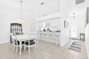 A modern kitchen with white cabinetry, a dining area with a white table and chairs, and a hallway leading to a door with a framed artwork. - Rotonda West Getaway | Private Heated Pool Retreat (Rotonda West)