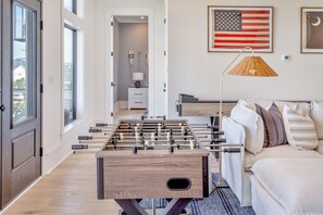 A room with a foosball table, a sofa, and an American flag on the wall. - Best Of Both Worlds: Views, Pool, Location & Luxury (Murrells Inlet)