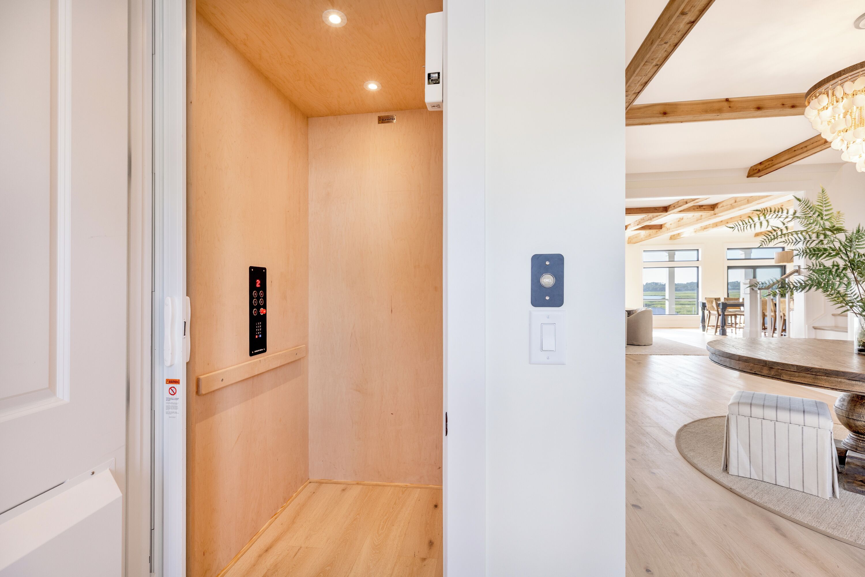 Ein modernes Interieur mit Holzboden, einem sichtbaren Aufzug und einem Essbereich mit rundem Tisch und Stühlen.