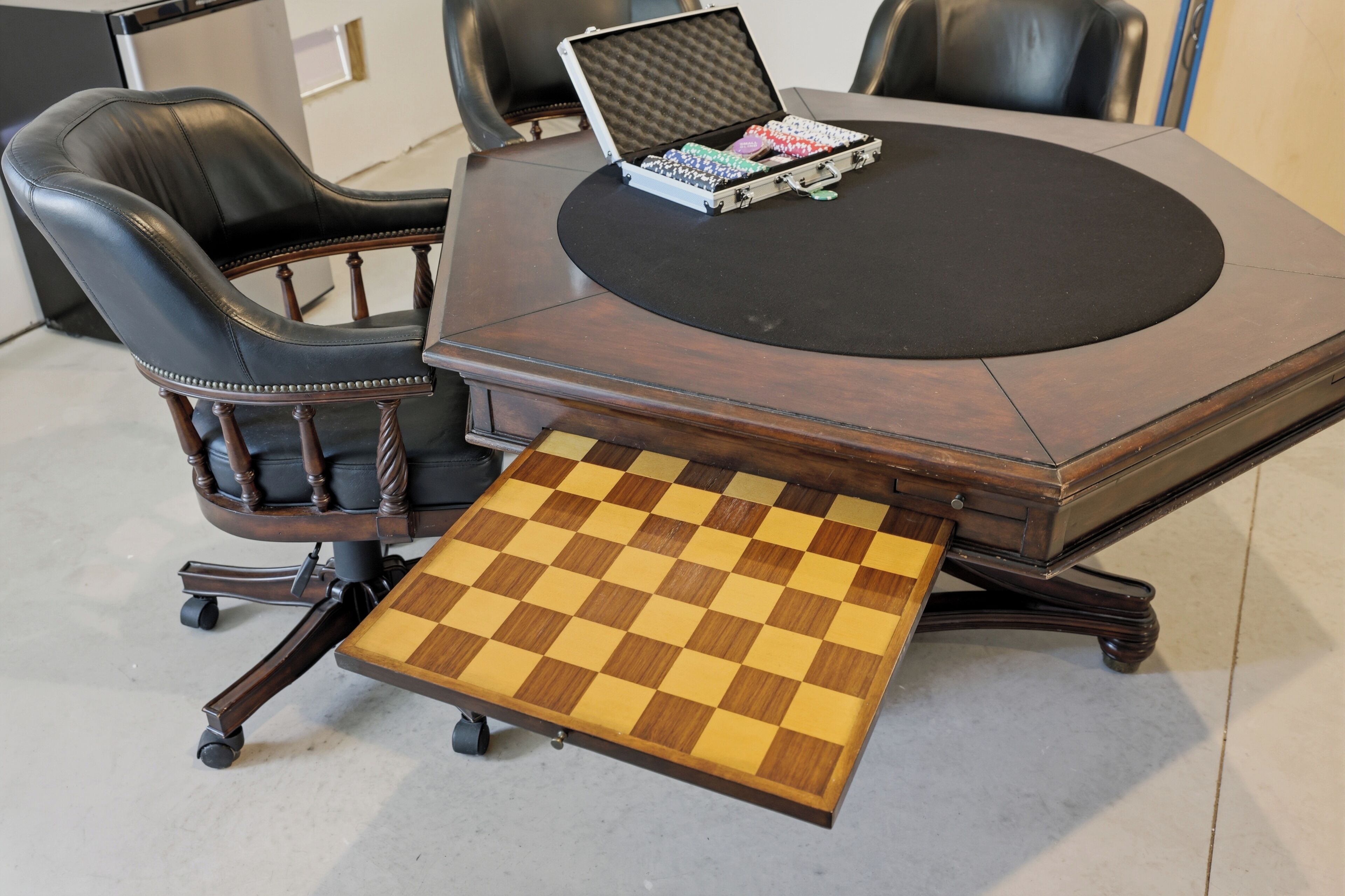 A round wooden table with a chessboard on a stand, leather chairs, and a briefcase with items on top.