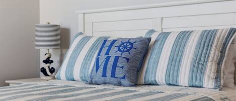 A bed with striped bedding and pillows, a white headboard, and a lamp with a figure on the nightstand.
