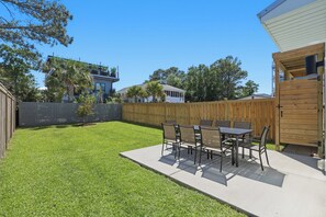 A backyard with a patio table and chairs, a wooden fence, and a house in the background. - Upscale New Construction 4BR/3BA Coastal Retreat • 3-Min Walk to Beach •Sleeps 9 (Carolina Beach)