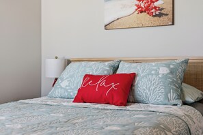 Een bed met een bedspreide met een patroon, twee kussens met een koraalrif ontwerp, en een aan de muur bevestigde lamp.