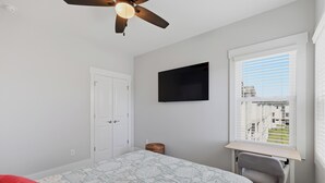 A bedroom with a bed, a desk, a chair, a ceiling fan, a TV, and a window with blinds. - Upscale New Construction 4BR/3BA Coastal Retreat • 3-Min Walk to Beach •Sleeps 9 (Carolina Beach)
