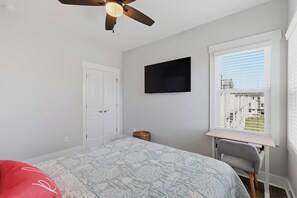 A bedroom with a bed, a desk, a chair, a ceiling fan, a TV, and a window with blinds. - Upscale New Construction 4BR/3BA Coastal Retreat • 3-Min Walk to Beach •Sleeps 9 (Carolina Beach)