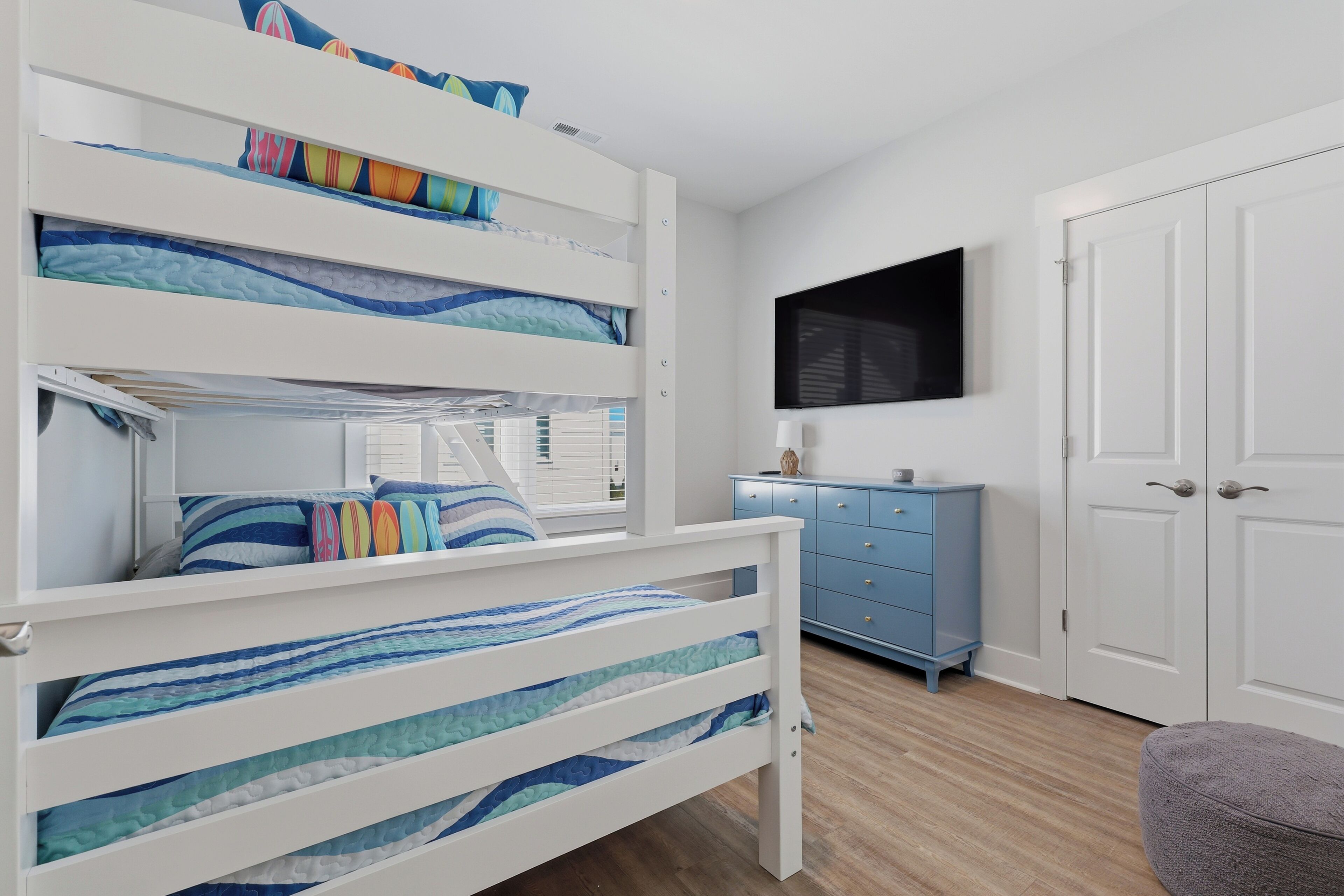 A bunk bed with wave-patterned bedding, a blue dresser, a flat-screen TV, and a closed door.