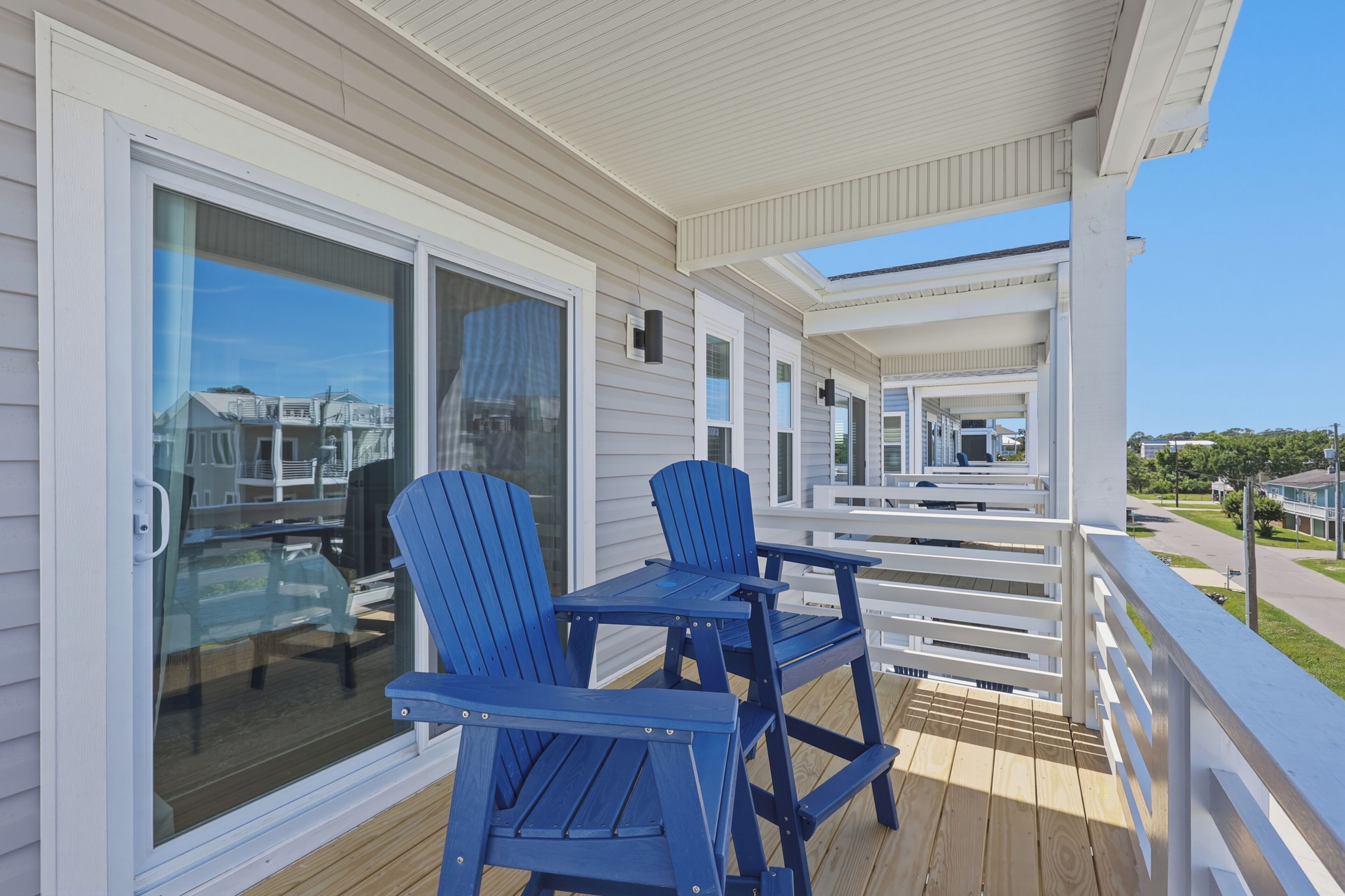 A covered outdoor deck with a table and two chairs, a sliding glass door, and a view of neighboring houses.