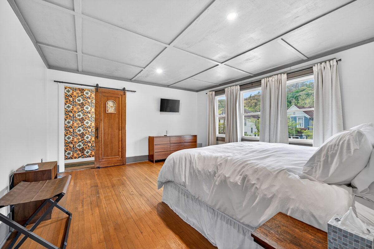 A bedroom with a bed, wooden desk, and a TV on the wall.