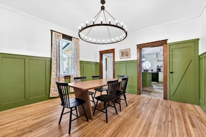 Ein Esszimmer mit Holztisch und -stühlen, einer Kristallleuchtre und grünen Wandverkleidungen.
