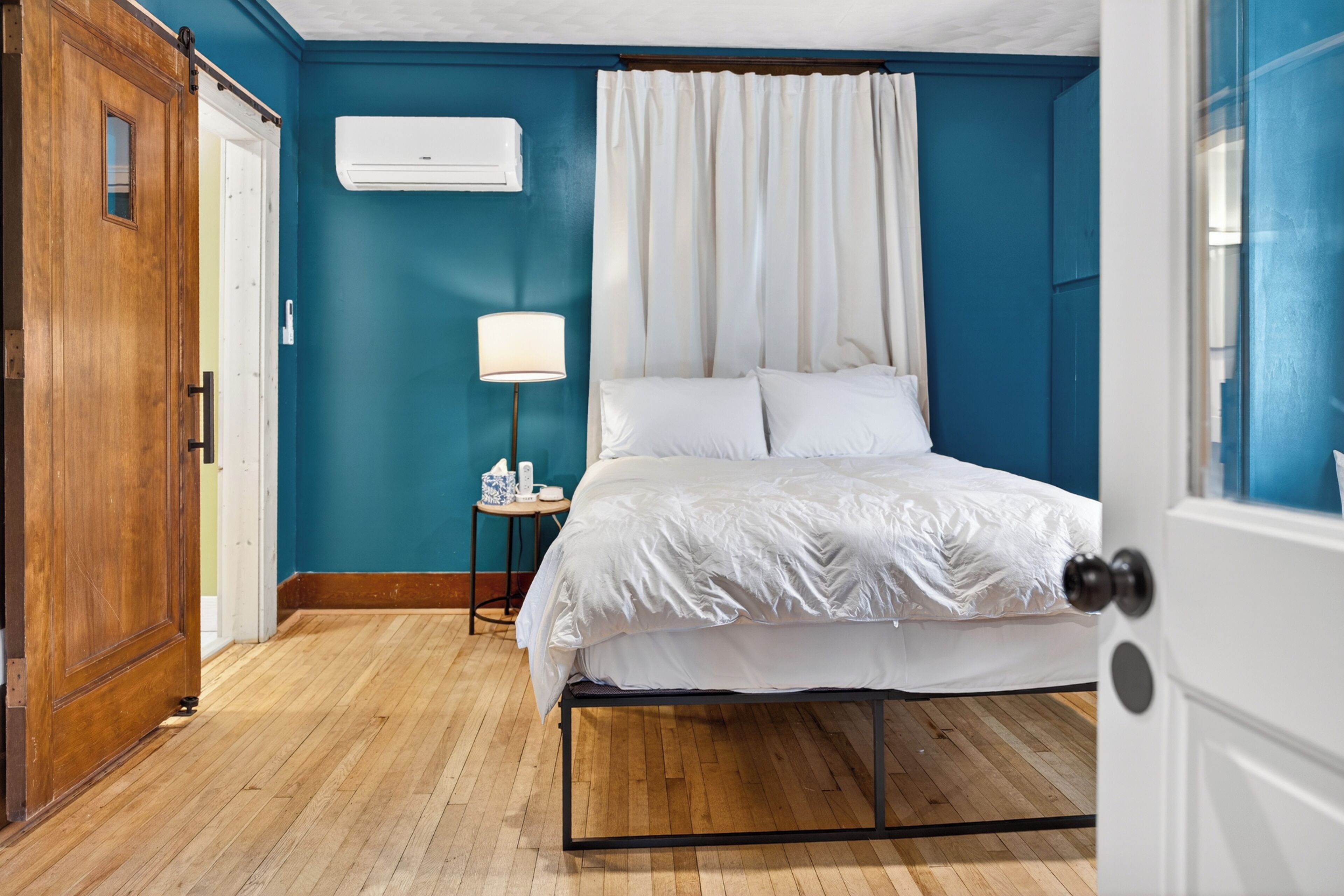 Un dormitorio con cama, mesita de noche, lámpara y un equipo de aire acondicionado en la pared.