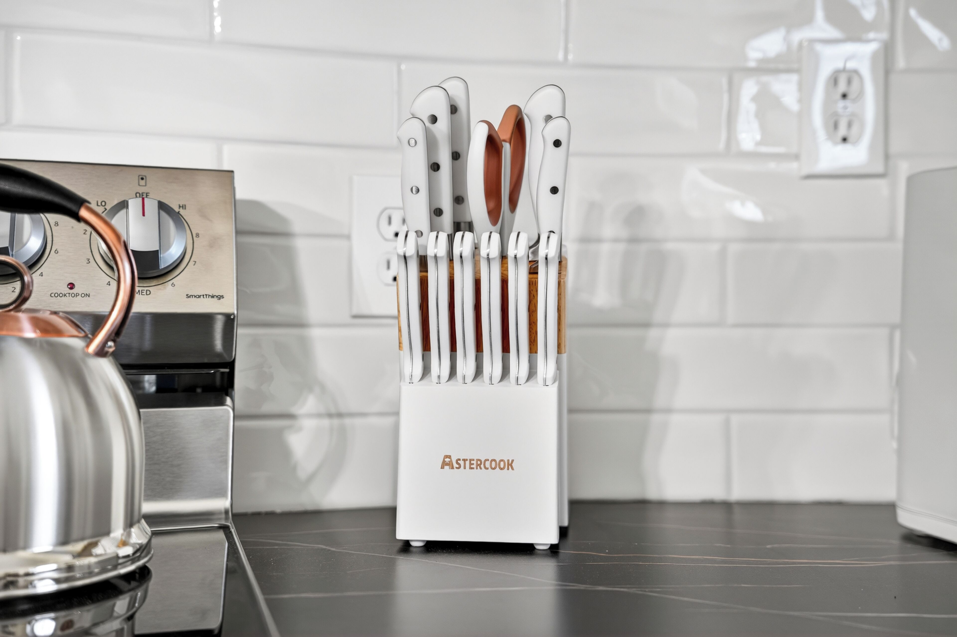 A kitchen with a modern stove, a kettle, and a knife block.