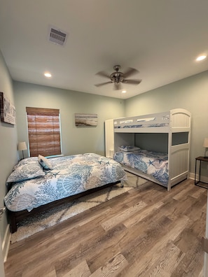 A bedroom with a bunk bed, a ceiling fan, a window with blinds, and a rug on the wooden floor. - House, 2 Masters, Hot Tub, Tiki & Game, Sleeps 12 (Bolivar Peninsula)