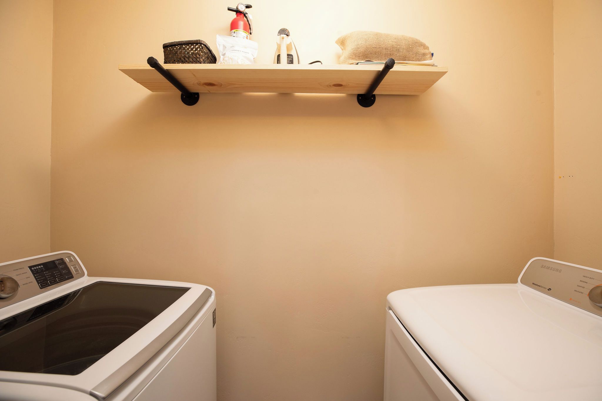 A laundry area with two washing machines, a shelf with a fire extinguisher, and a basket.