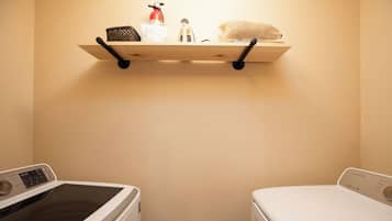 A laundry area with two washing machines, a shelf with a fire extinguisher, and a basket.